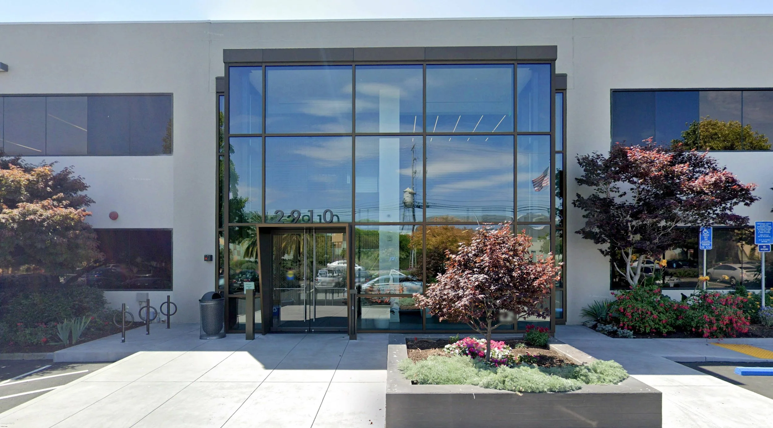 Modern commercial building with large glass windows, landscaped flower beds, and handicap parking signs outside.