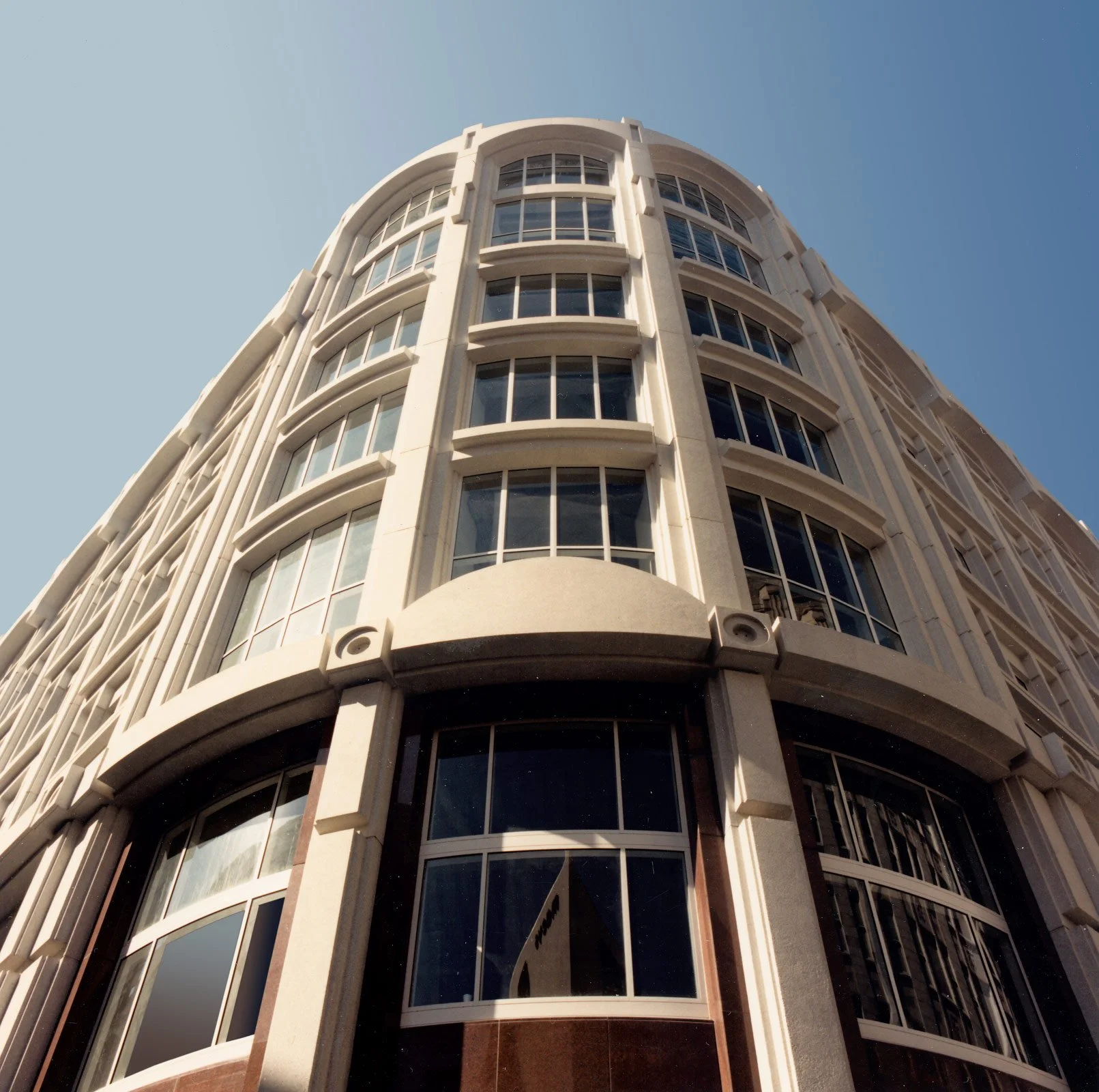 Low-angle view of a tall modern building with curved architecture and large glass windows against a clear blue sky.
