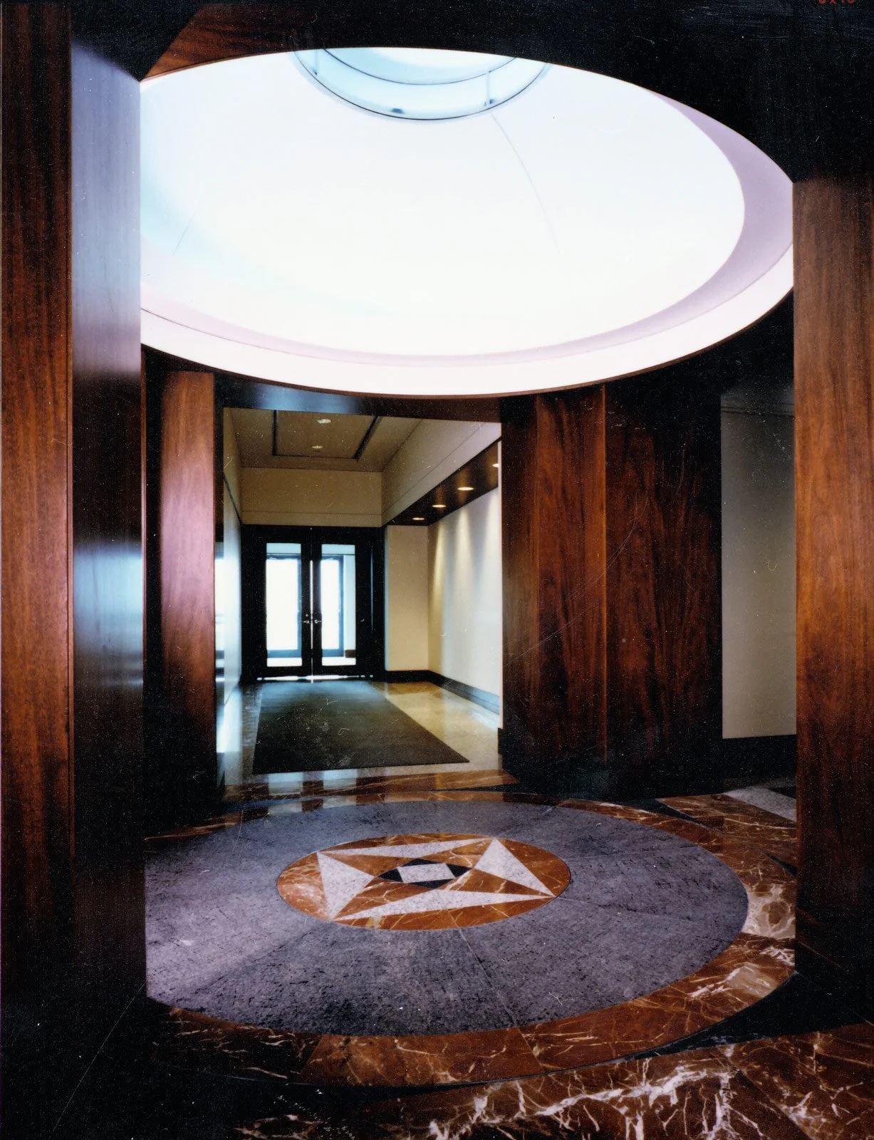 Interior view of a doorway with wooden framing, a circular marble floor design with a star shape in the center, and a large round skylight overhead.