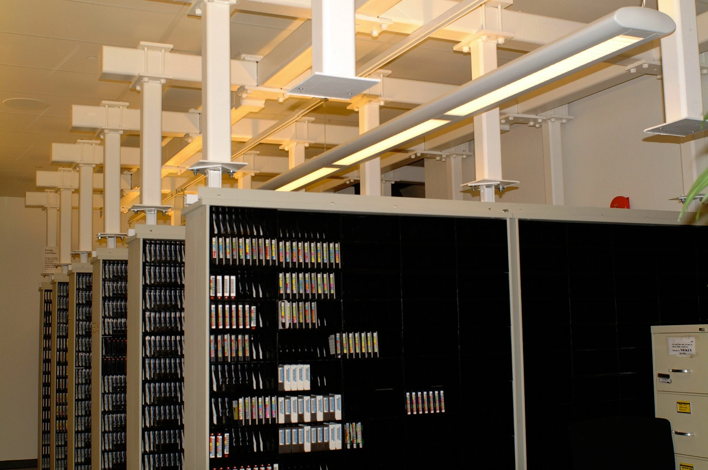 Library with black bookshelves filled with books, ceiling with white structural beams and lighting fixtures