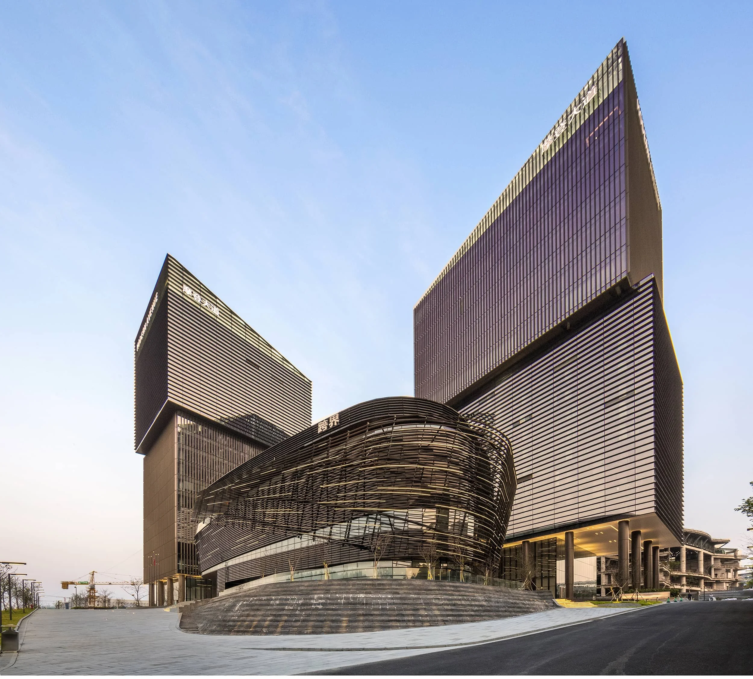 Modern hospital building with two large glass towers and a rounded central structure, set against a clear blue sky.
