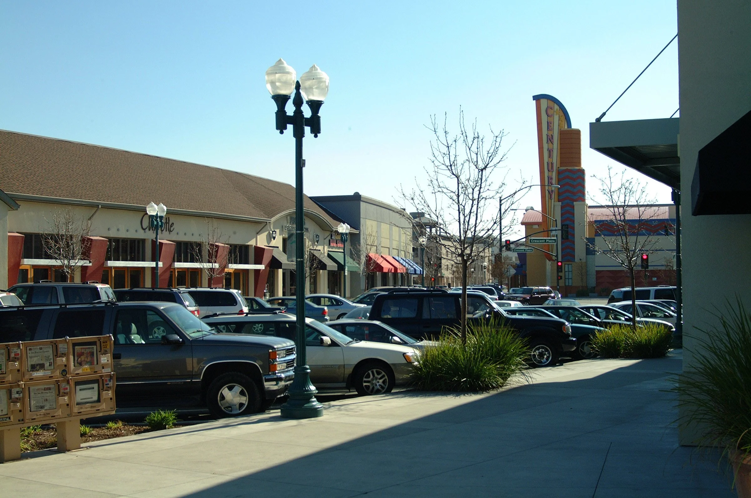 Parking lot with cars, storefronts, street signs, and a tall neighborhood