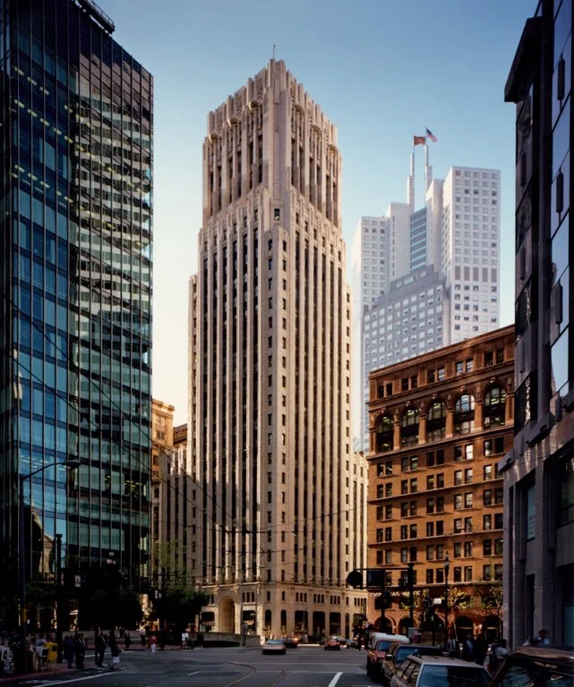 A tall, historic skyscraper surrounded by modern glass buildings on a city street during daytime.