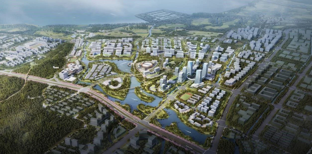 Aerial view of a planned urban development with modern buildings, water features, parks, and roads near a body of water.