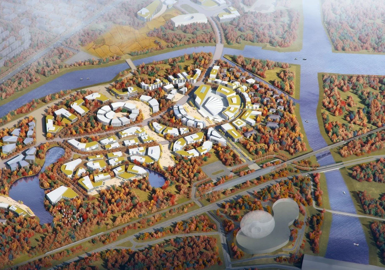 Aerial view of a planned urban development with various modern buildings, surrounded by water bodies, bridges, and greenery with colorful autumn trees.