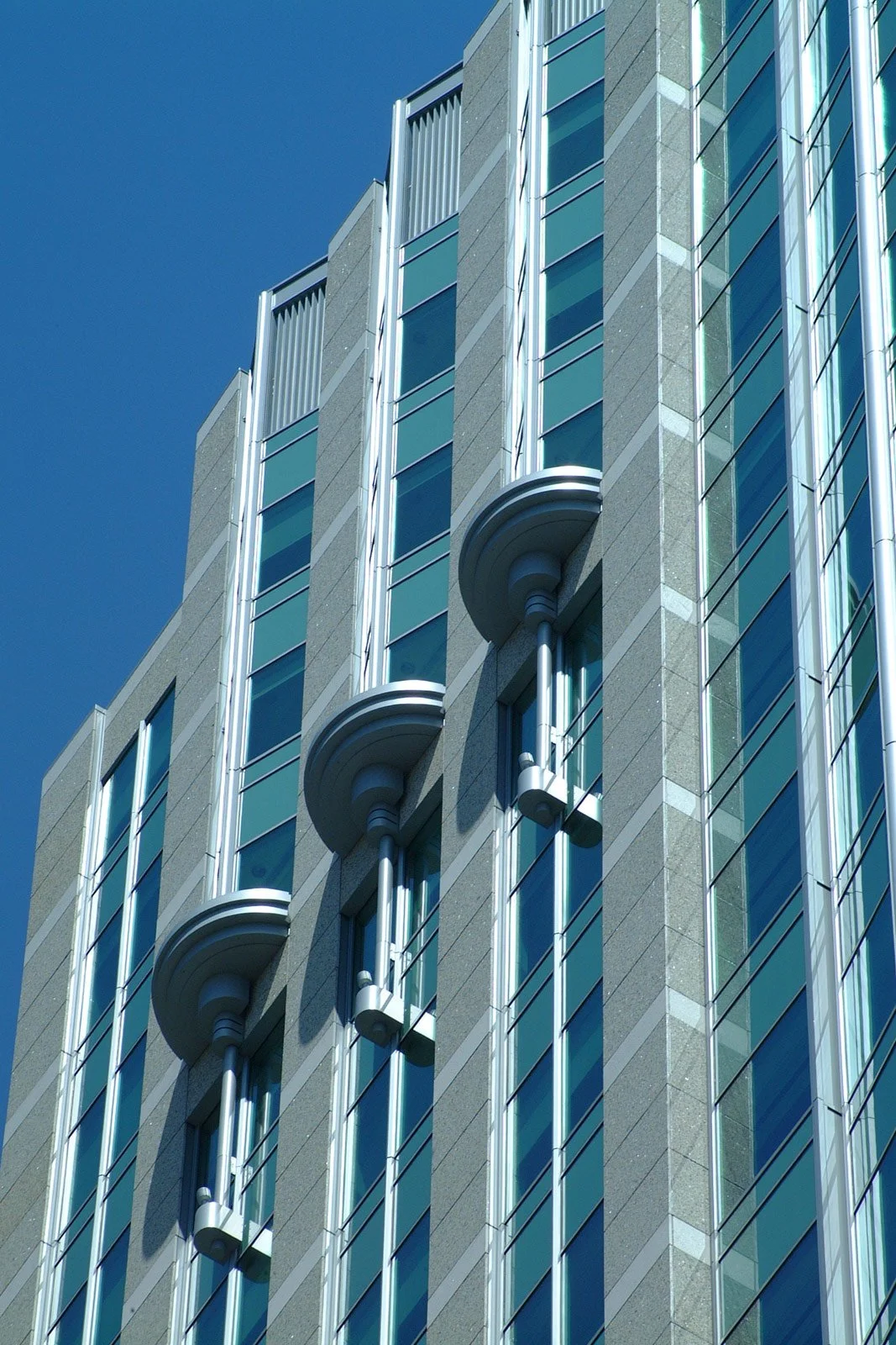 Close-up view of a modern building's exterior with large glass windows and metal architectural details against a clear blue sky.
