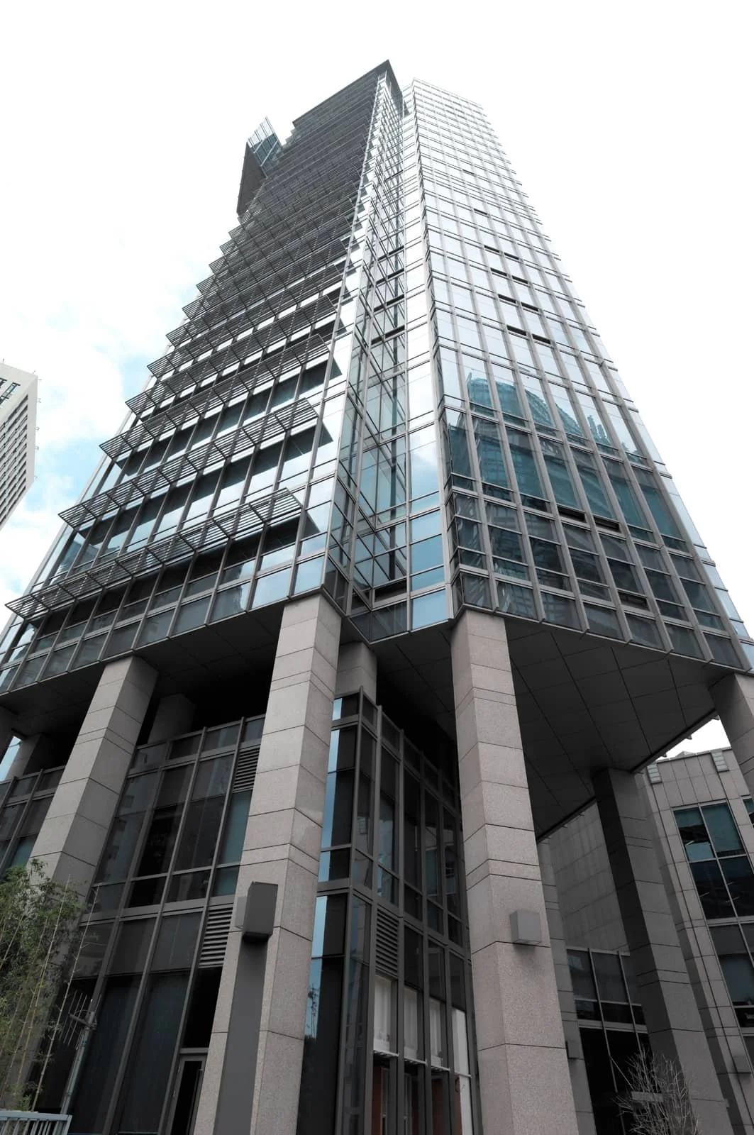 A modern glass skyscraper seen from a low angle, with reflective windows and geometric design in an urban setting.