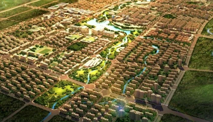 Aerial view of a planned urban development featuring green parks, water bodies, and residential buildings arranged in a grid pattern.