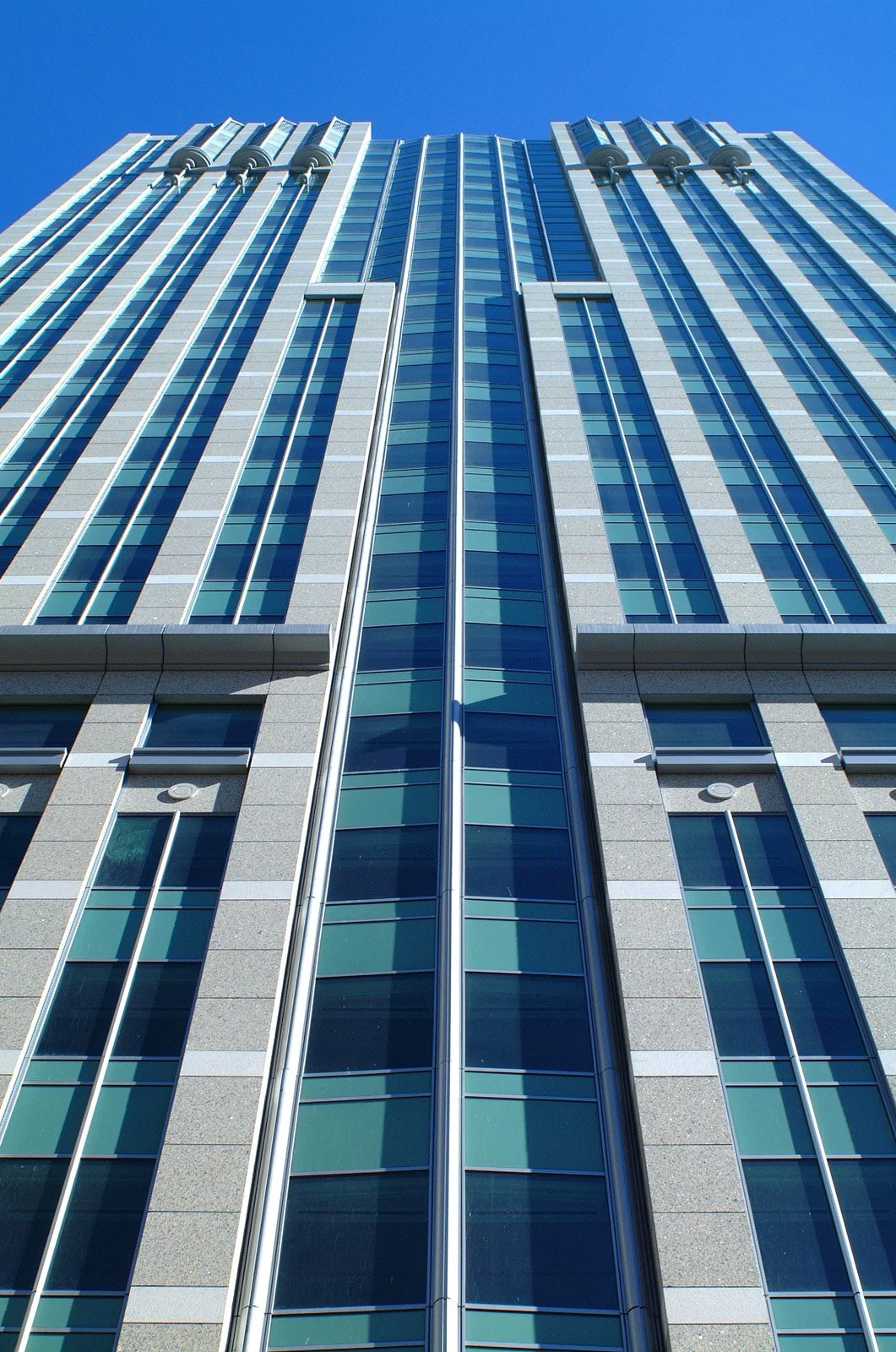 Low-angle view of a modern skyscraper with glass windows reflecting the blue sky.