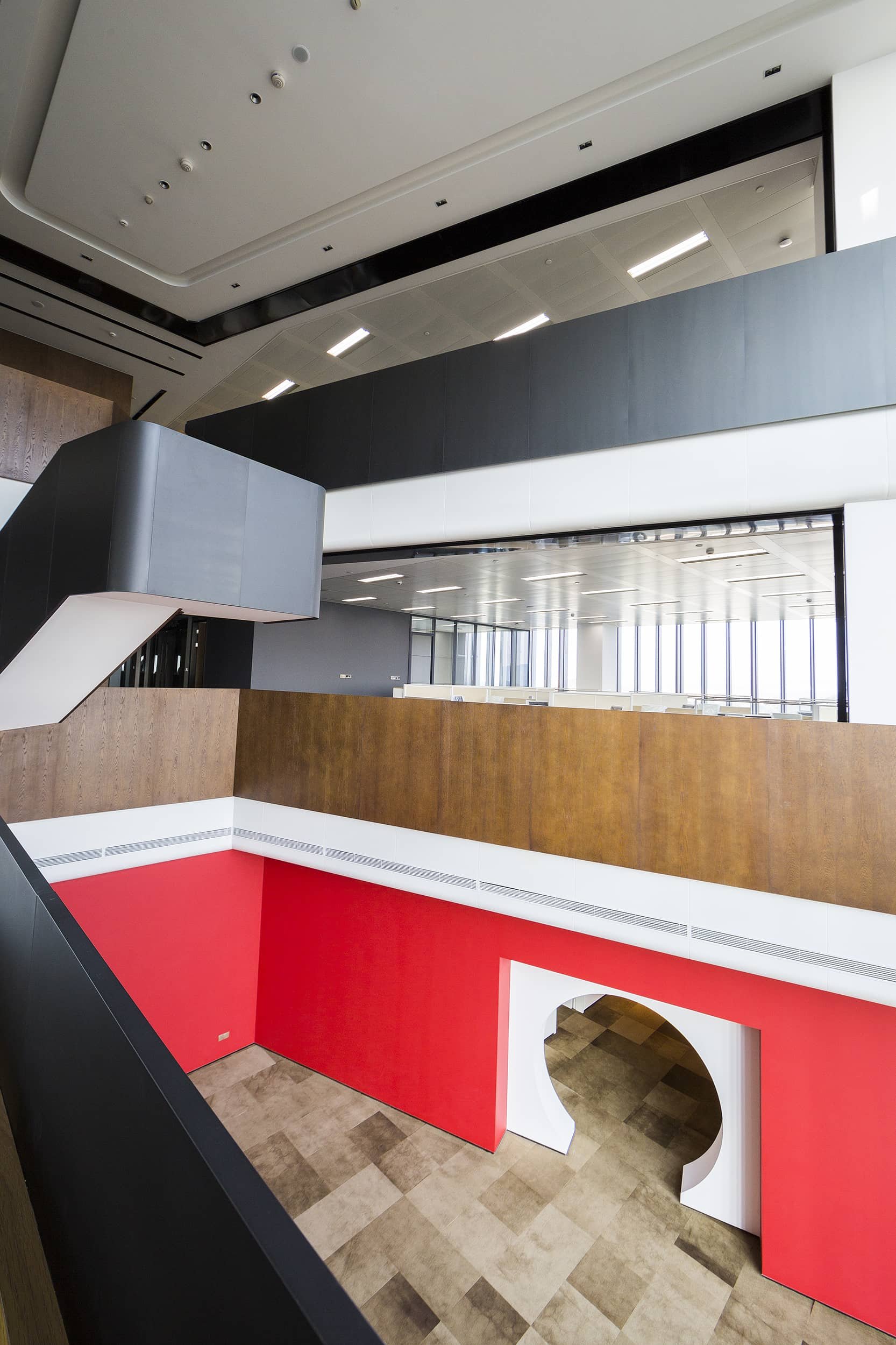 Interior of a modern building with a curved staircase, colorful walls, wood paneling, large windows, and multiple levels with open spaces.