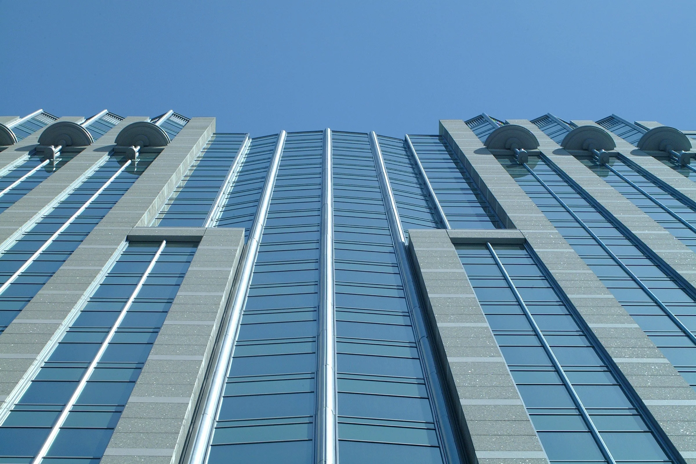 Low-angle view of a modern skyscraper with glass windows and metal accents under a clear blue sky.
