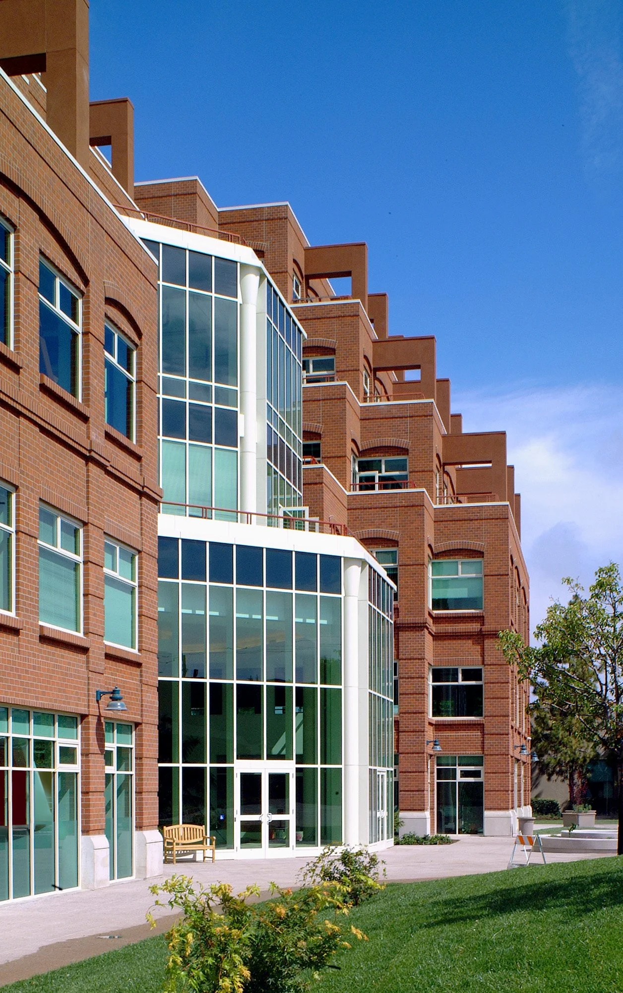 Multi-story brick building with large glass-section entrance, surrounded by a lawn and trees.