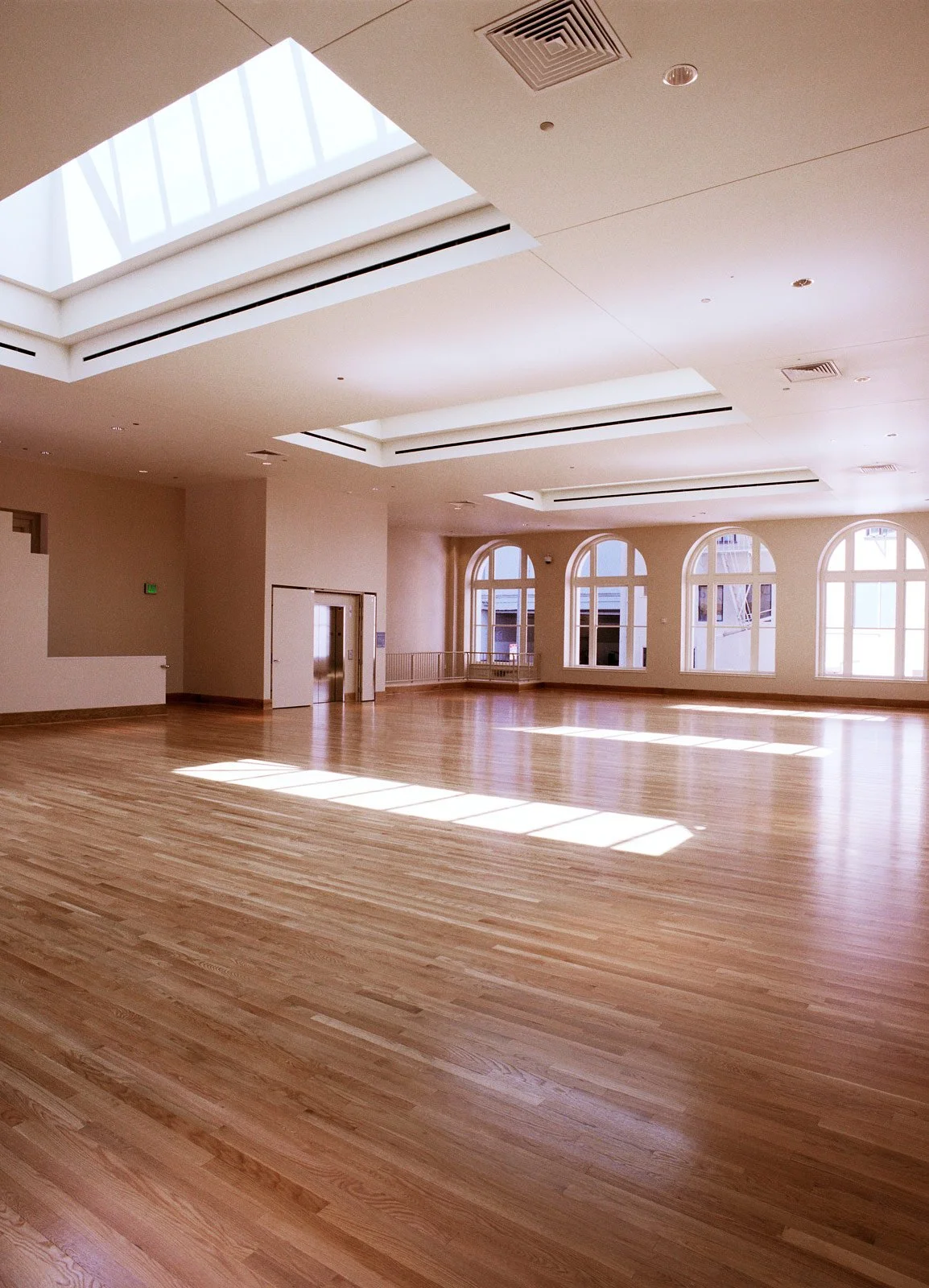 Empty spacious room with large arched windows, wooden floors, and skylights allowing natural light to fill the space.