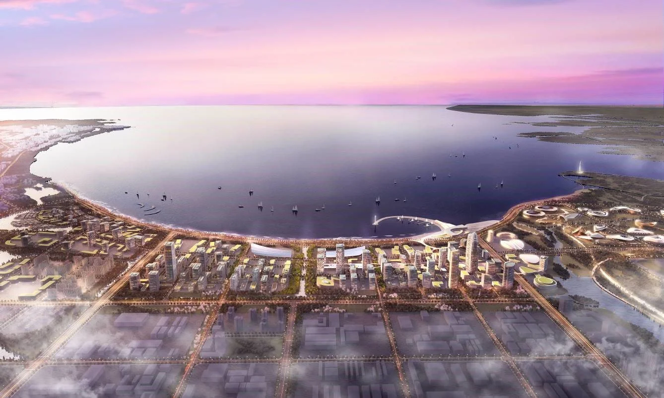 Aerial view of a modern city with skyscrapers near a large body of water, with sailboats on the water and a pink and purple sunset sky.