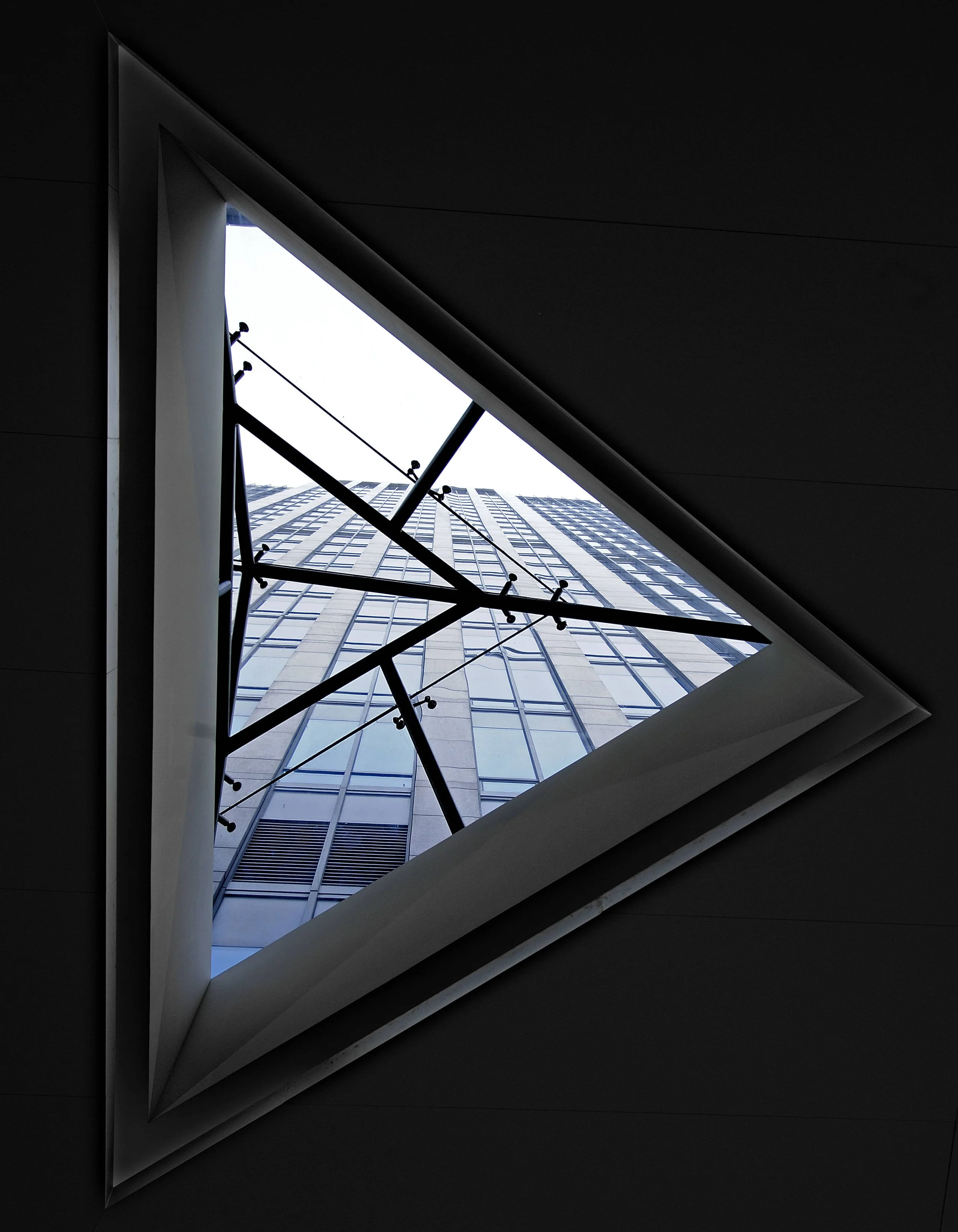 Looking up through a square skylight at a modern high-rise building with glass windows and a metal framework.
