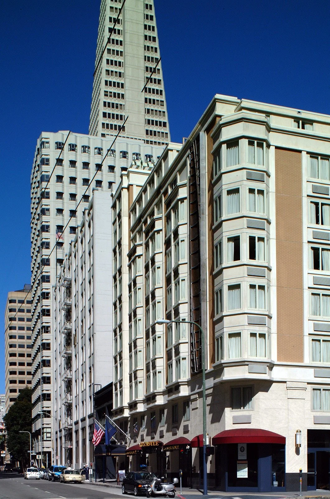 Downtown street view with tall buildings and a restaurant on the ground level, under a clear blue sky.