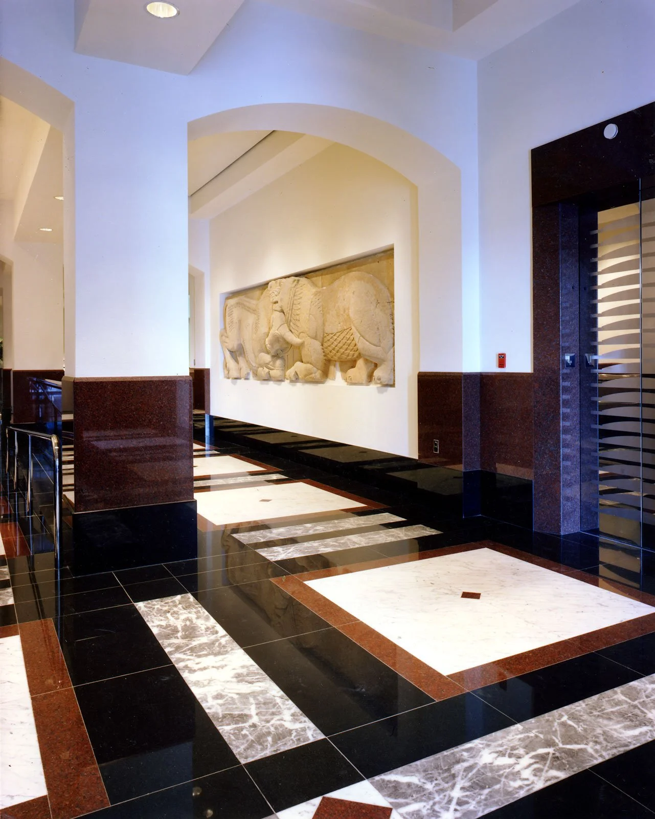 Hotel lobby with black, white, and red marble floor, white walls, a carved stone elephant relief on the wall, and an elevator with striped design.