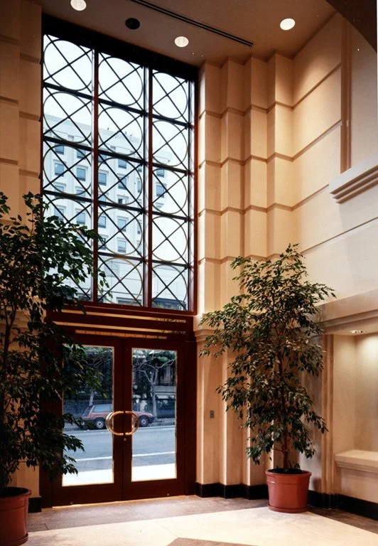 Interior of a modern lobby with tall windows, potted plants, and wooden accents.