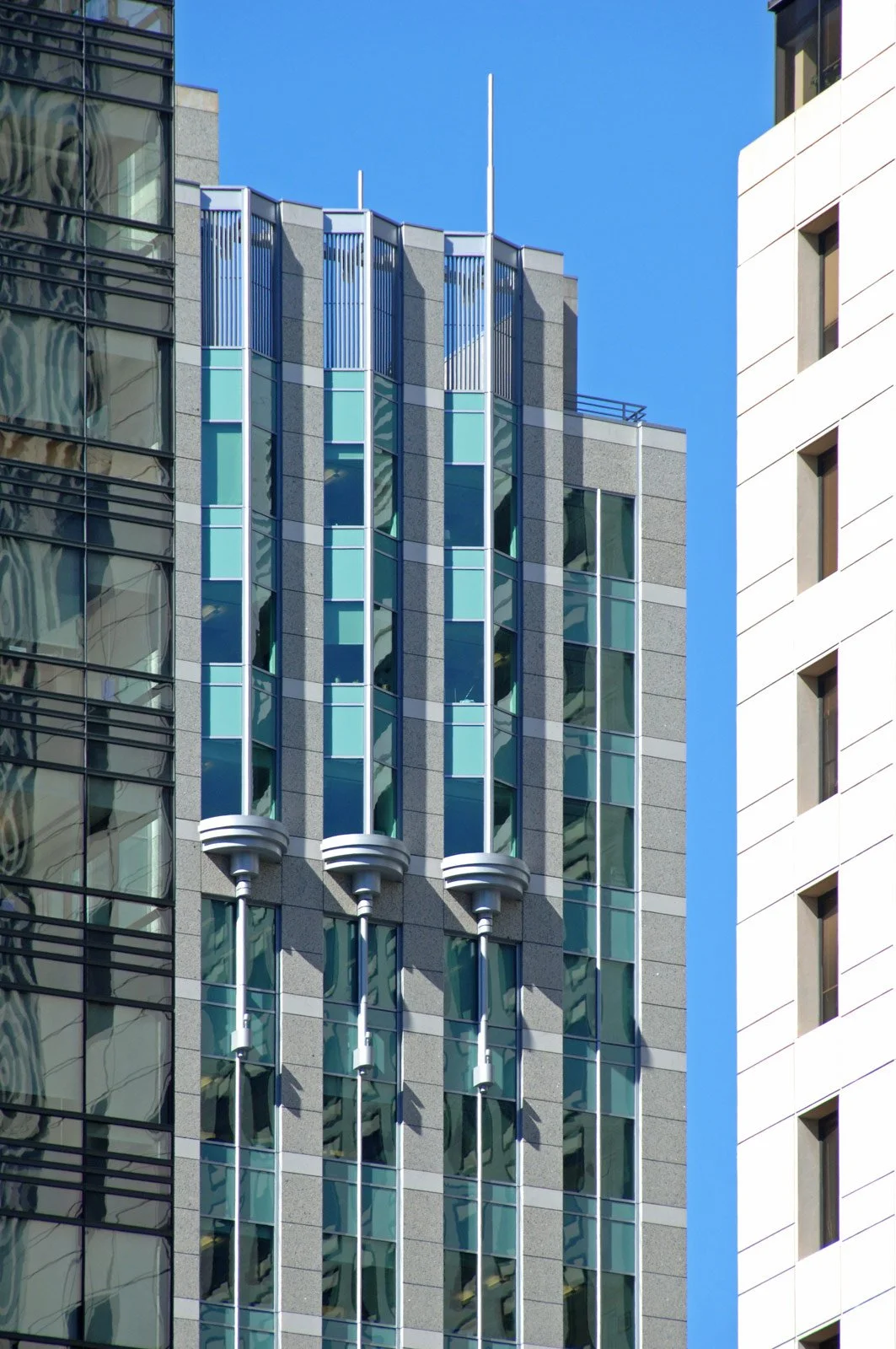Modern glass and concrete high-rise building with vertical metal fins and a blue sky background.