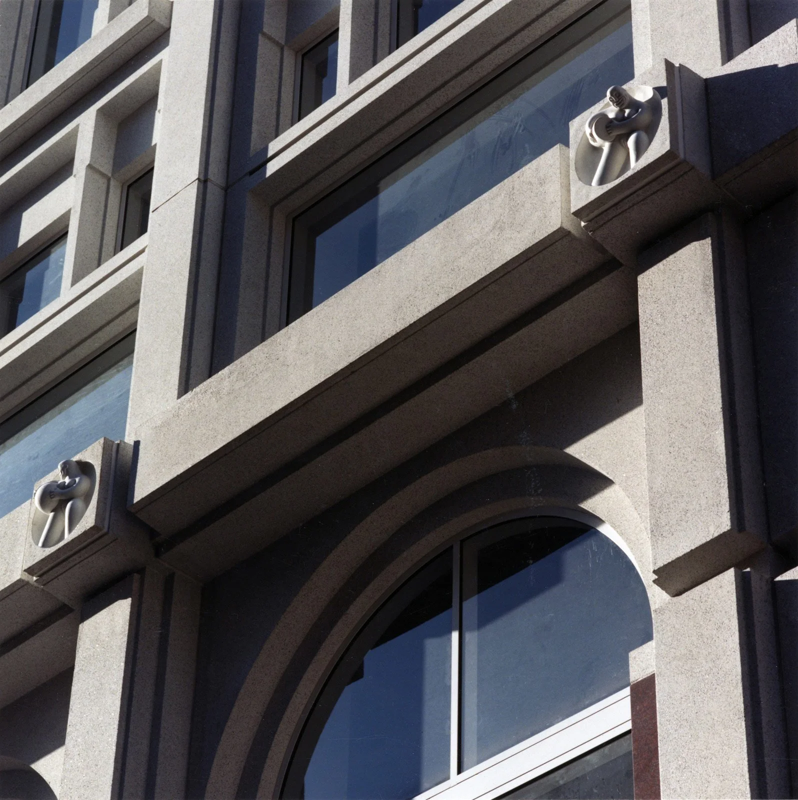 Close-up of a building's exterior with decorative sculptures on the corners and large arched windows.