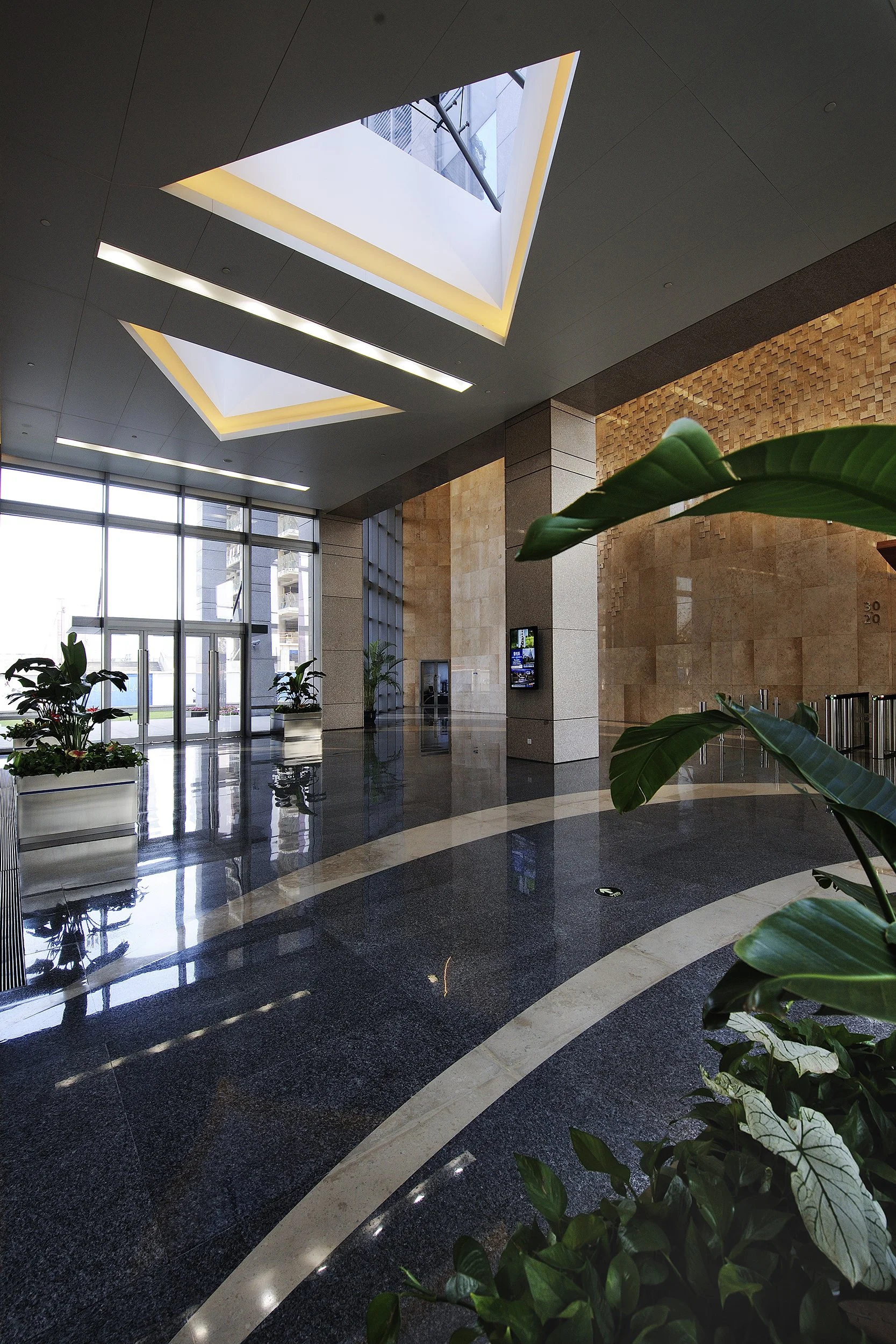 Modern building lobby with large glass doors, indoor plants, and skylights in the ceiling.
