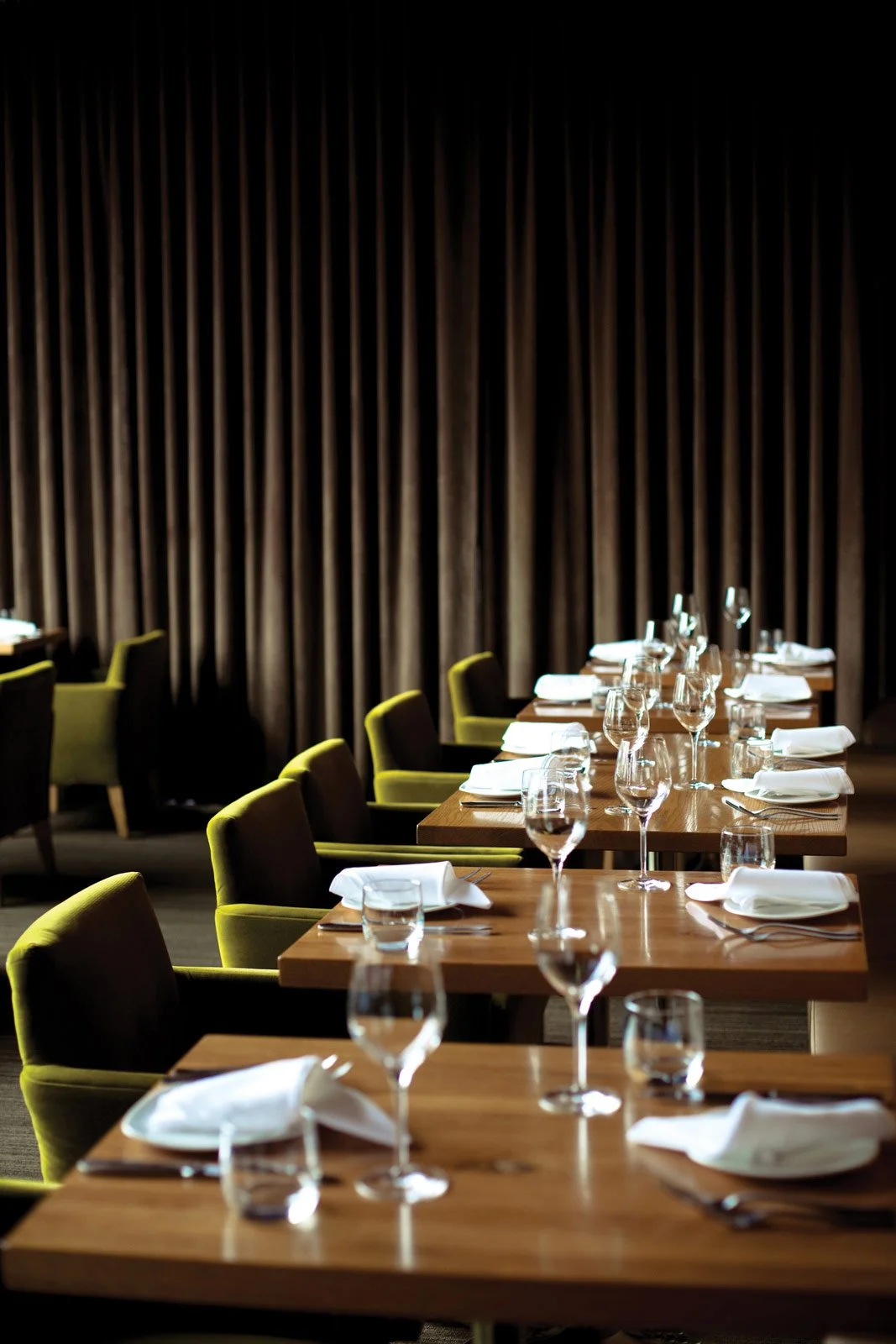 Elegantly set restaurant table with wine glasses, water glasses, white napkins, and silverware, with dark curtains in the background.