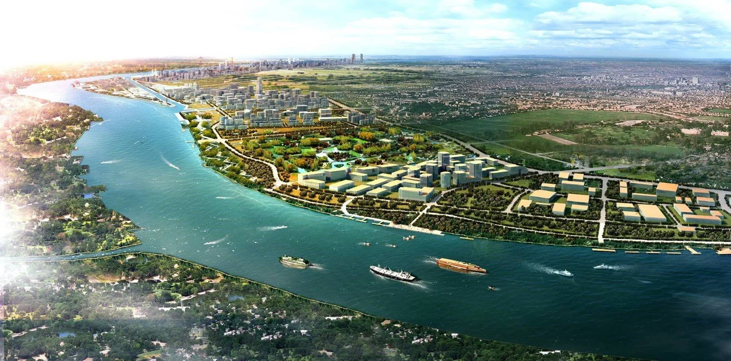 Aerial view of a large river with boats, a city skyline, and a green park area with buildings and roads surrounding the river.