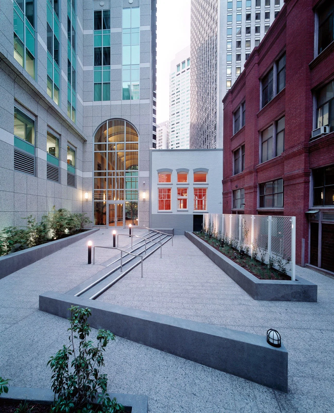 Urban rooftop courtyard with interconnected ramps, garden beds, surrounding tall modern and historic buildings, and decorative lighting.