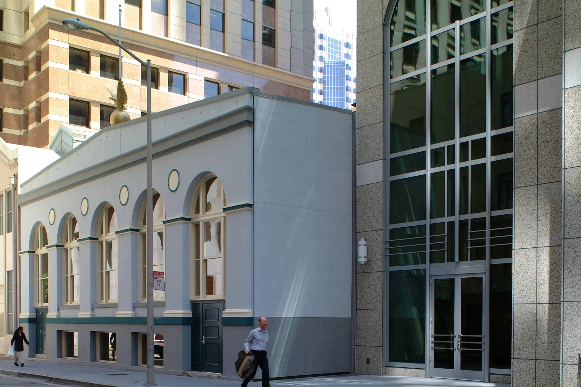 City street scene with pedestrians, modern and historic buildings, streetlamp, and a man walking with a briefcase.