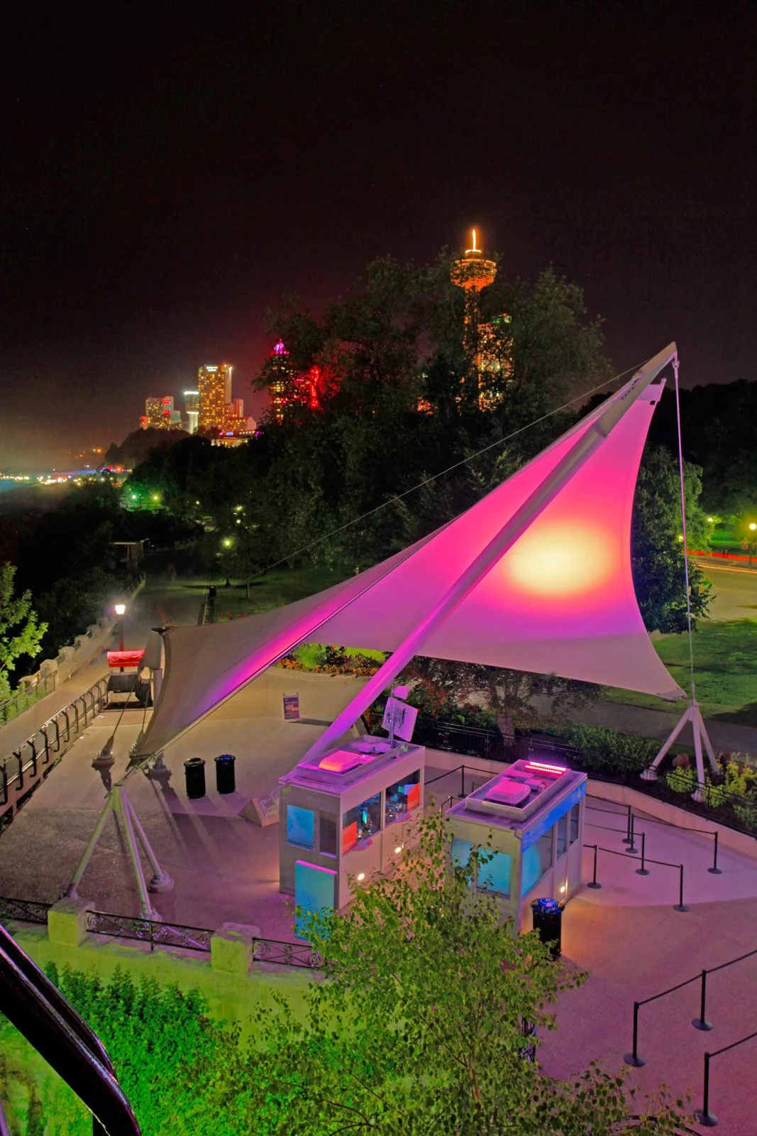 Night view of Pink's Hot Dogs stand at the Santa Monica Pier with city skyline in the background, illuminated with colorful lights.