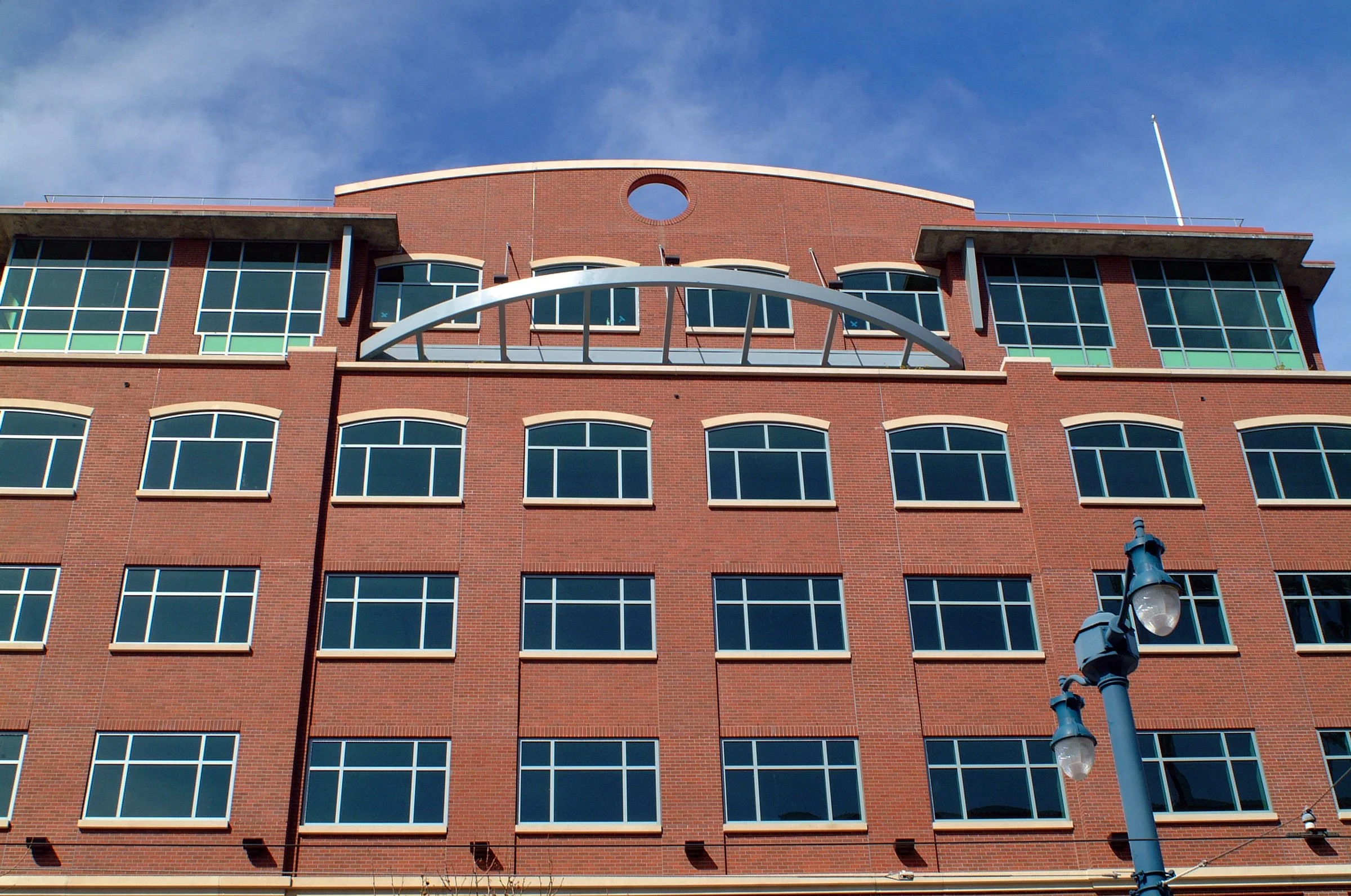 Red brick multistory building with numerous windows, a blue sky overhead, and a streetlamp in the foreground.