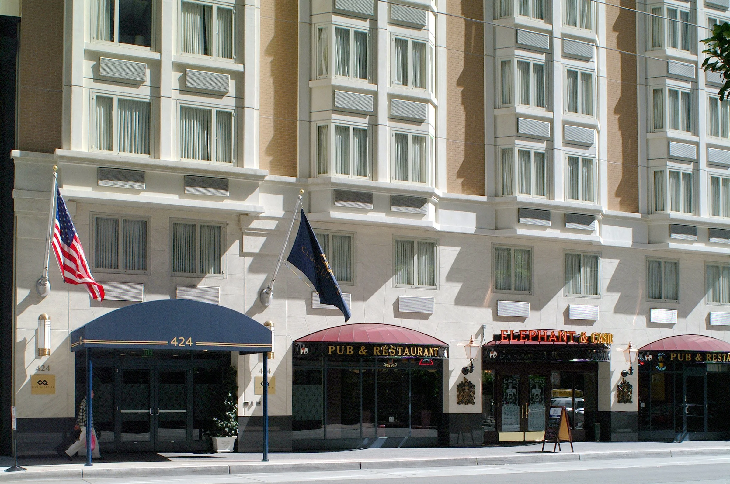 Facade of a building with signs for a pub and restaurant called Elephant & Castle, featuring an entrance with a blue awning, flags, and windows above.