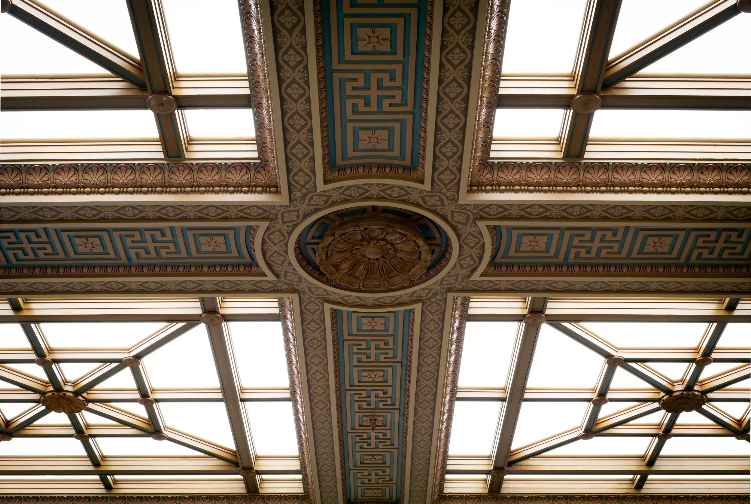 Ornate ceiling with decorative moldings, geometric patterns, and skylights.