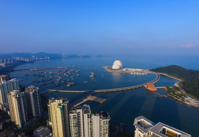 Aerial view of a city skyline near the water with tall buildings, a body of water with boats, a bridge, and a distinctive white dome building on a small island.