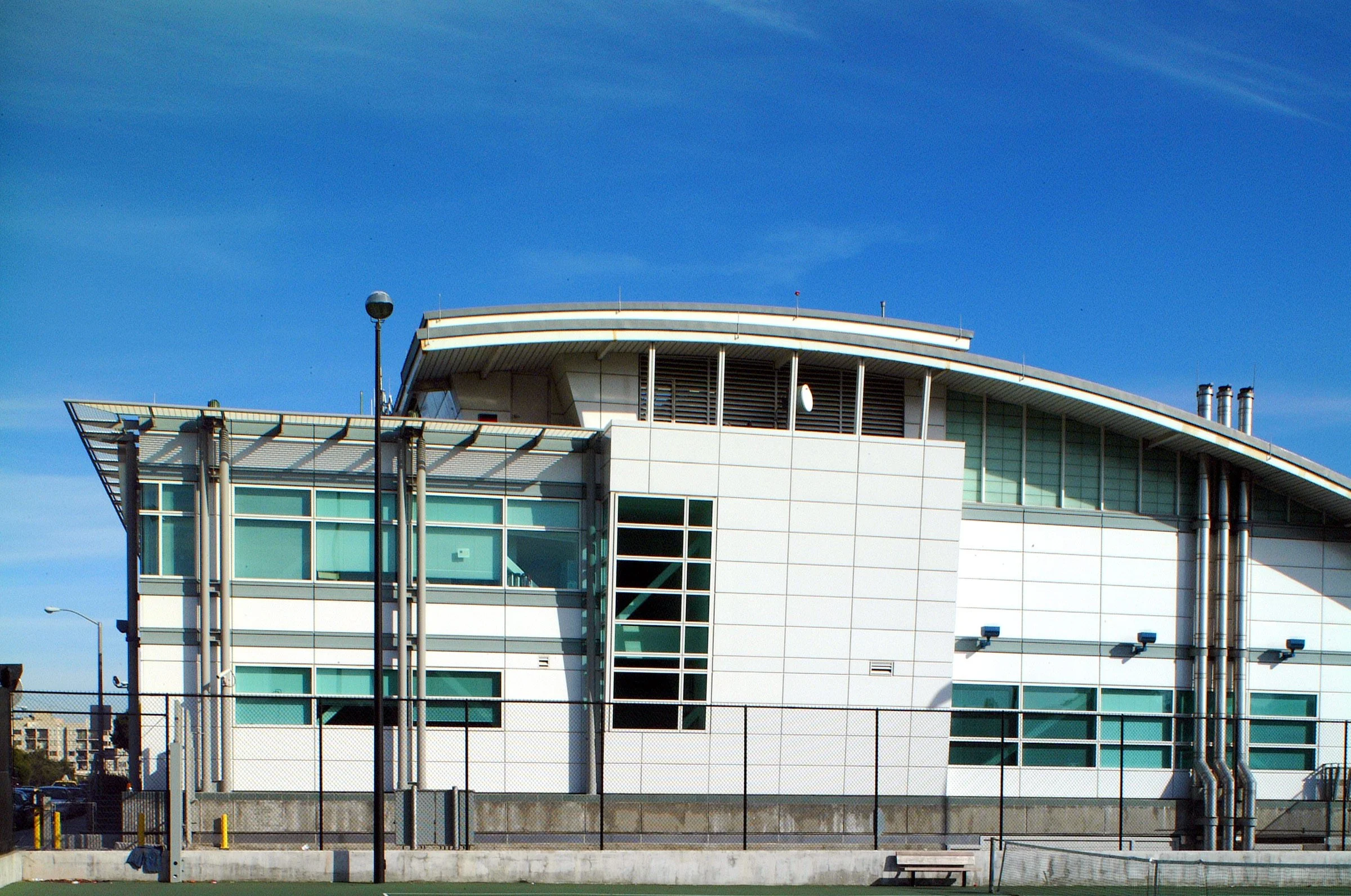 Modern sports stadium with white exterior, glass windows, and metal pipes, under a clear blue sky.