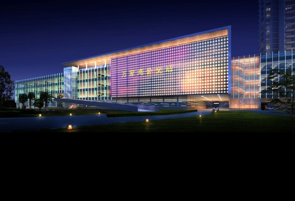 Modern multi-story building illuminated at night with a large LED screen displaying colorful light patterns, surrounded by trees and a well-lit driveway.