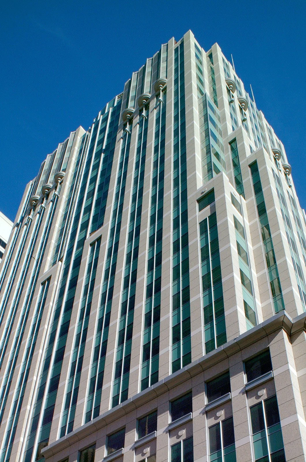 A tall modern skyscraper with glass windows and beige panels, viewed from below against a bright blue sky.
