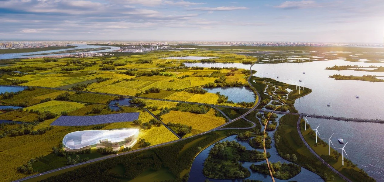 Aerial view of a green landscape with fields, water bodies, and wind turbines, with a city skyline in the distance under a partly cloudy sky.