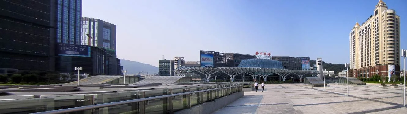 Cityscape with modern buildings and a large glass-covered transportation hub, sunny day with clear blue sky.