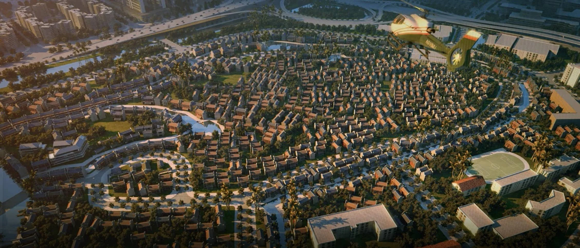 Aerial view of a suburban neighborhood with numerous houses, trees, and sports fields, with a yellow helicopter flying above at sunset.