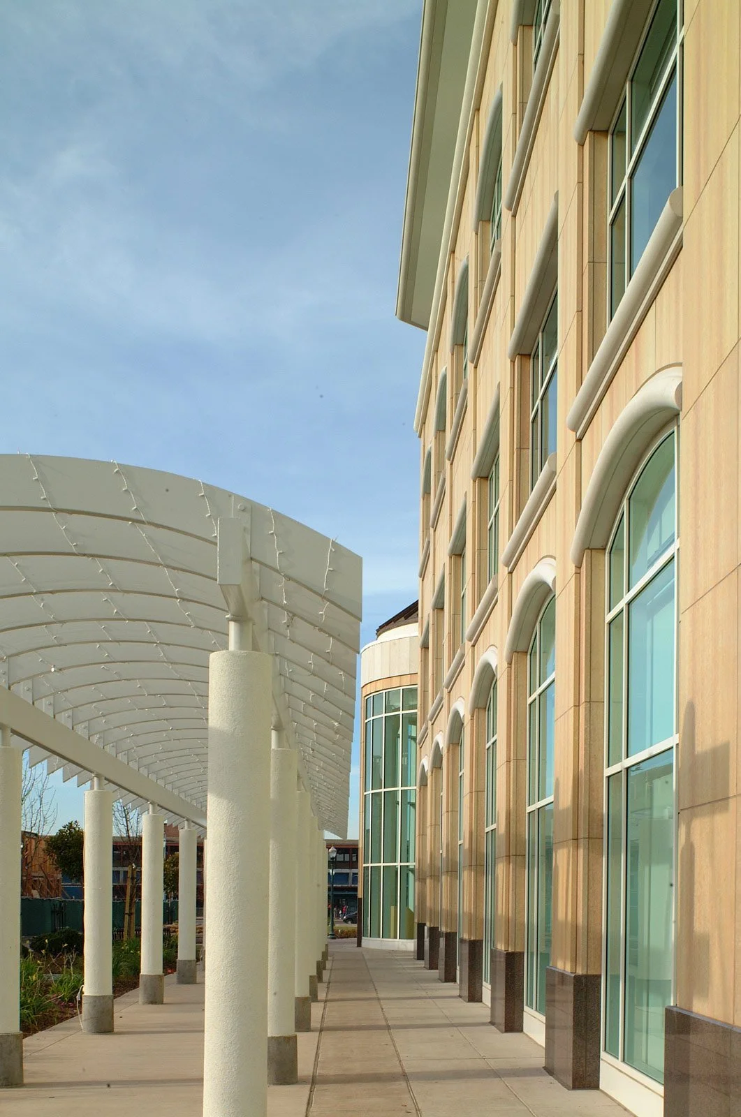 Modern building exterior with large windows and a covered walkway with white pillars, under a blue sky.