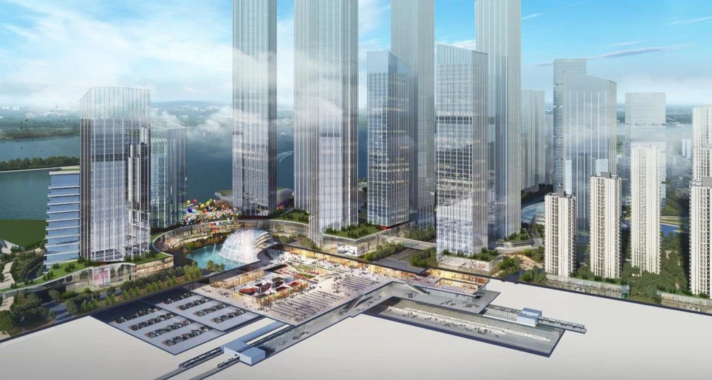 A modern city skyline with tall glass skyscrapers, a waterway, and a large transportation hub with parking and train tracks visible.