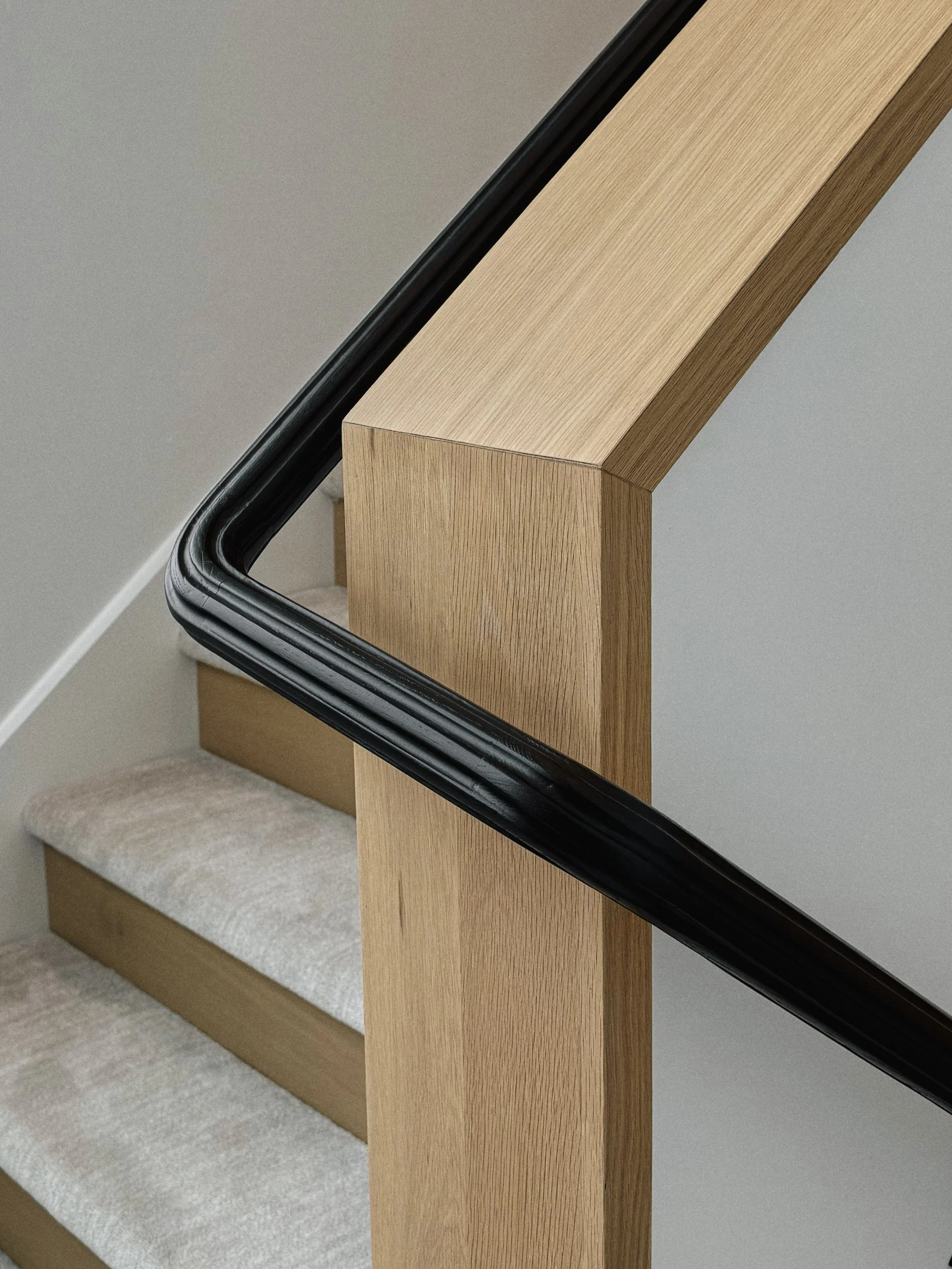 A close-up view of a staircase with wooden handrail, black trim, and beige carpeted steps.