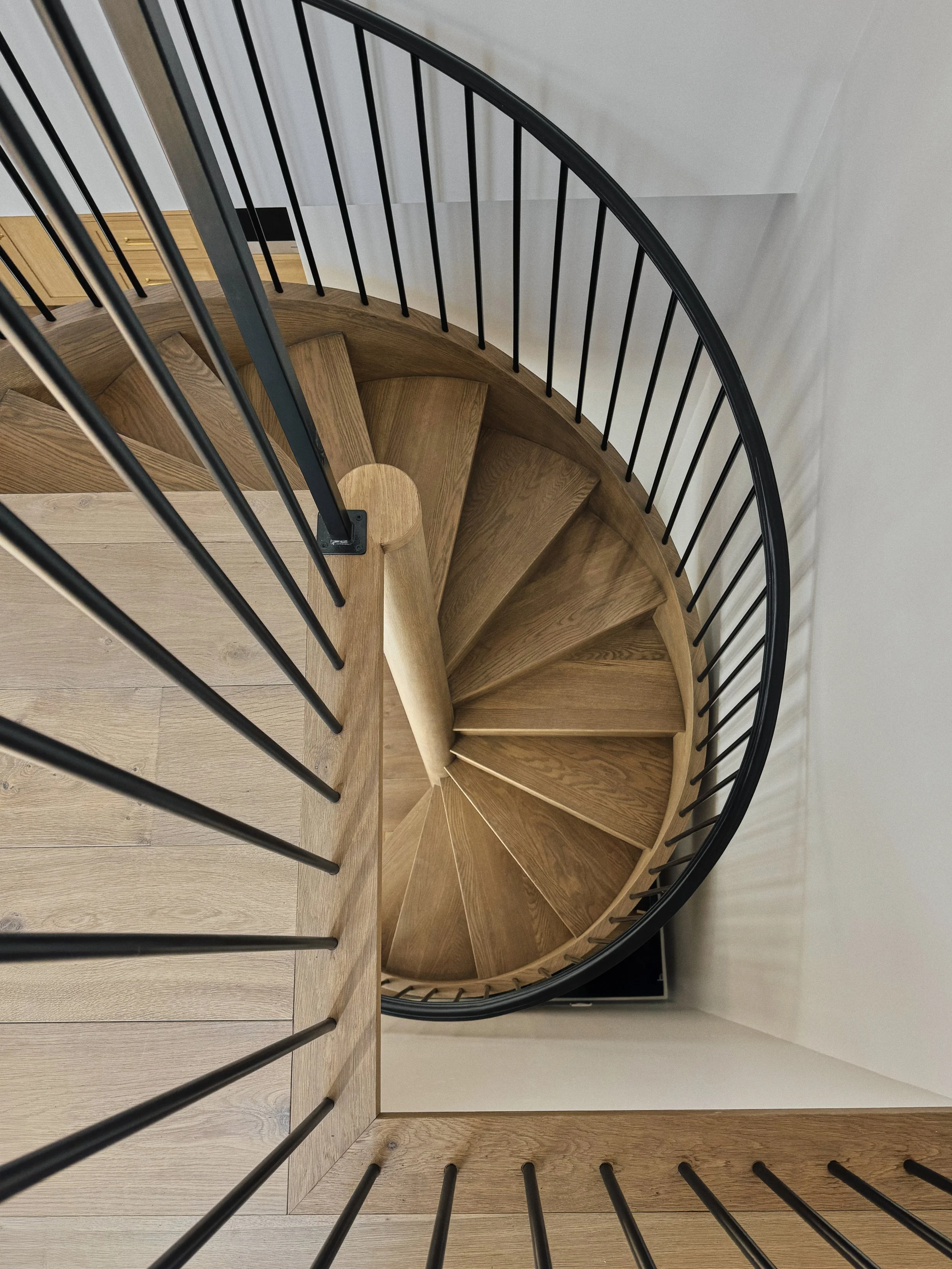 Top-down view of a wooden spiral staircase with black iron railings.