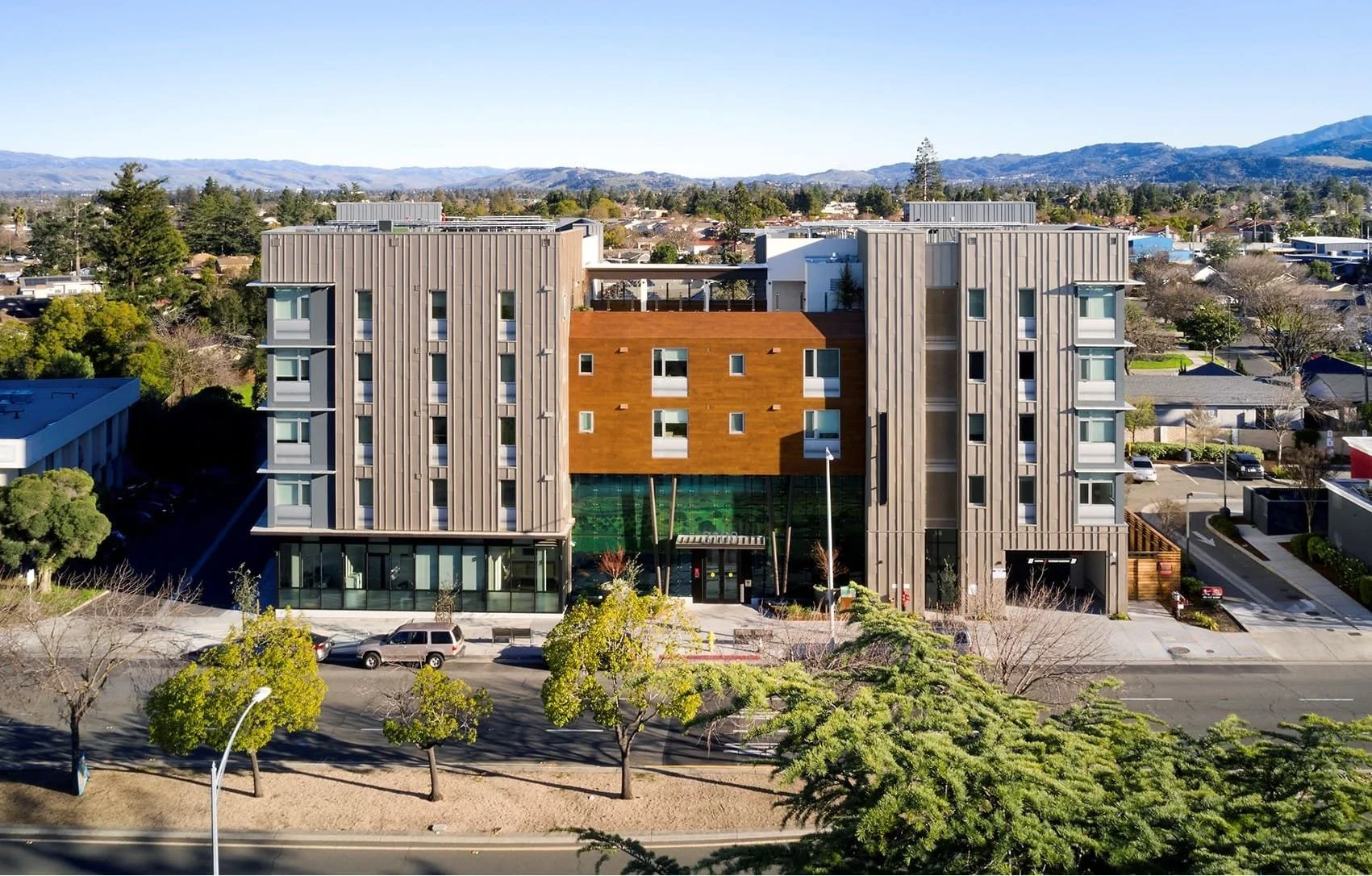 Vitalia: a modern multi-story apartment building with a mix of gray and wood exterior finishes, large glass windows, and a landscaped sidewalk.