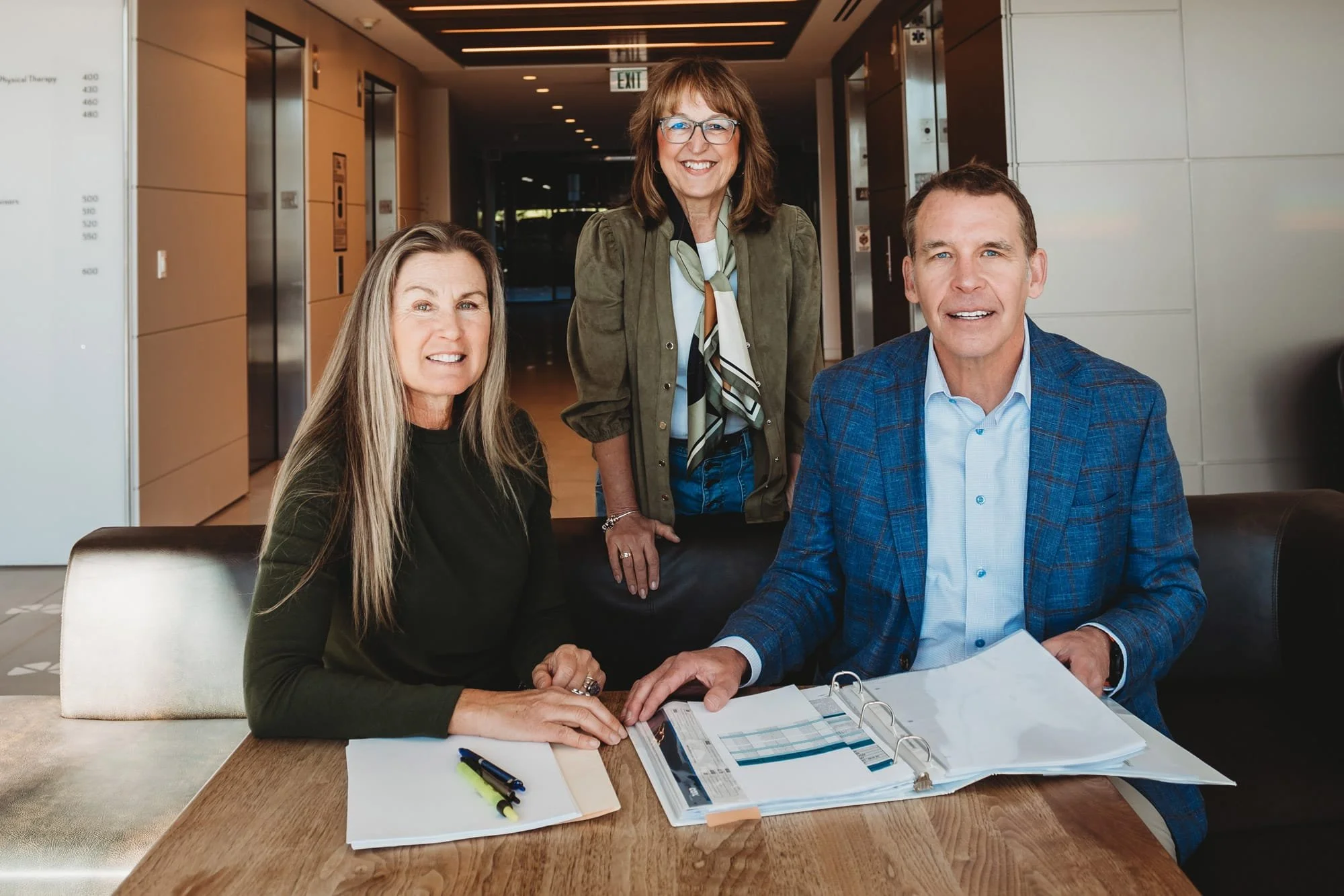 Robin Martinez, Nicki Cometa, and Jim Laverty sitting at a table in an office, going through documents and smiling.