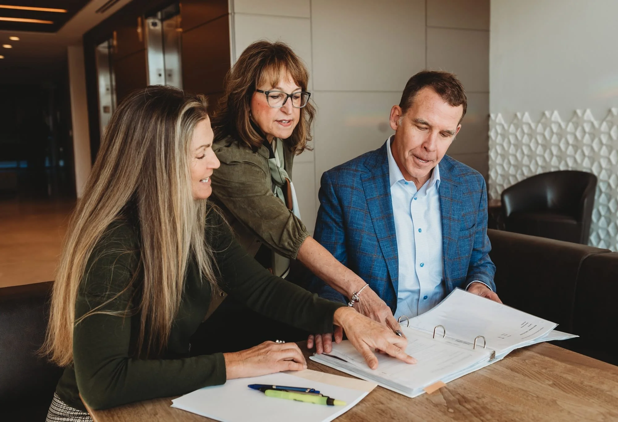 Robin Martinez, Nicki Cometa, and Jim Laverty look at documents on a table in an office space.