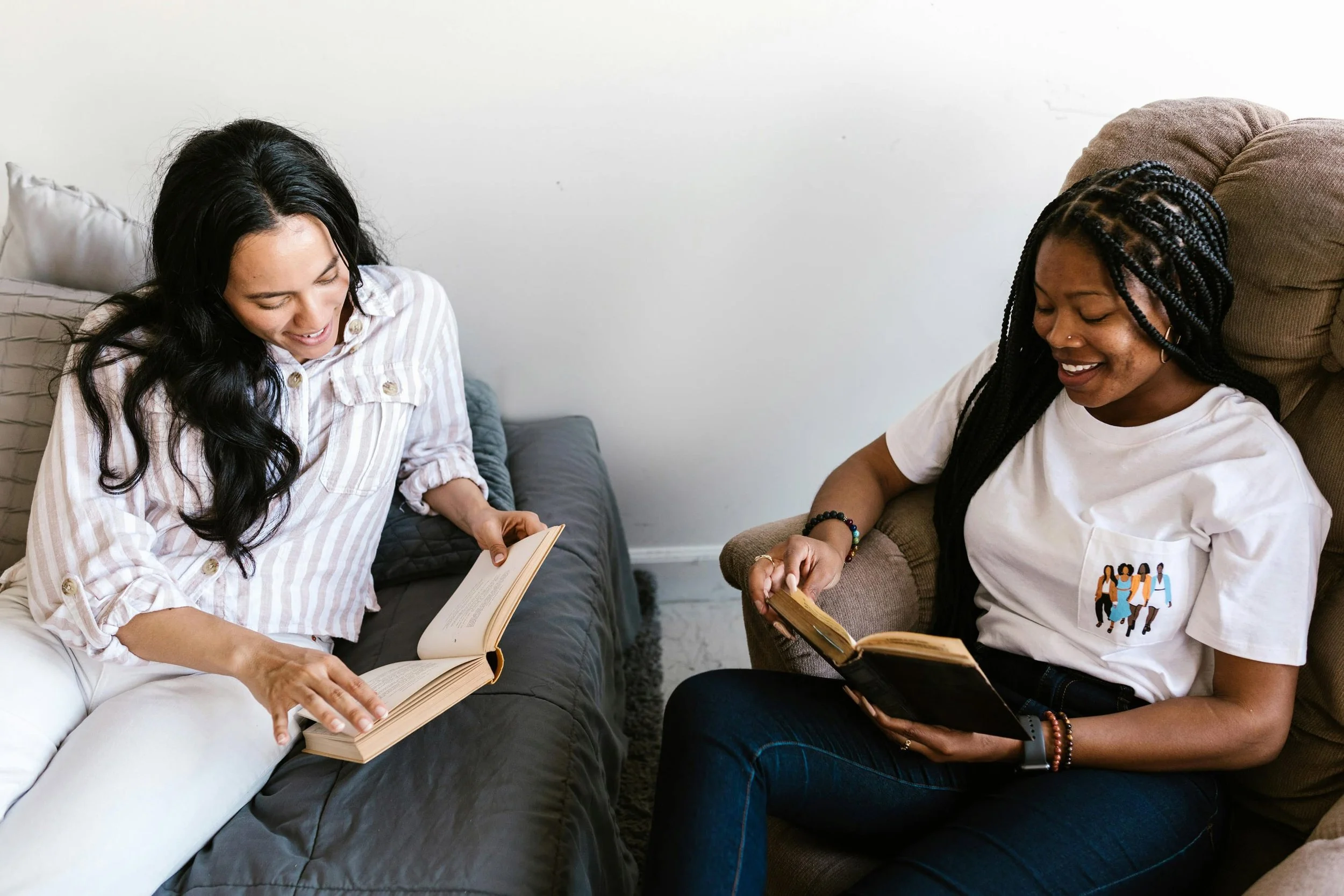 Two residents at a book club event, sitting on sofas, reading books and smiling in a cozy space.