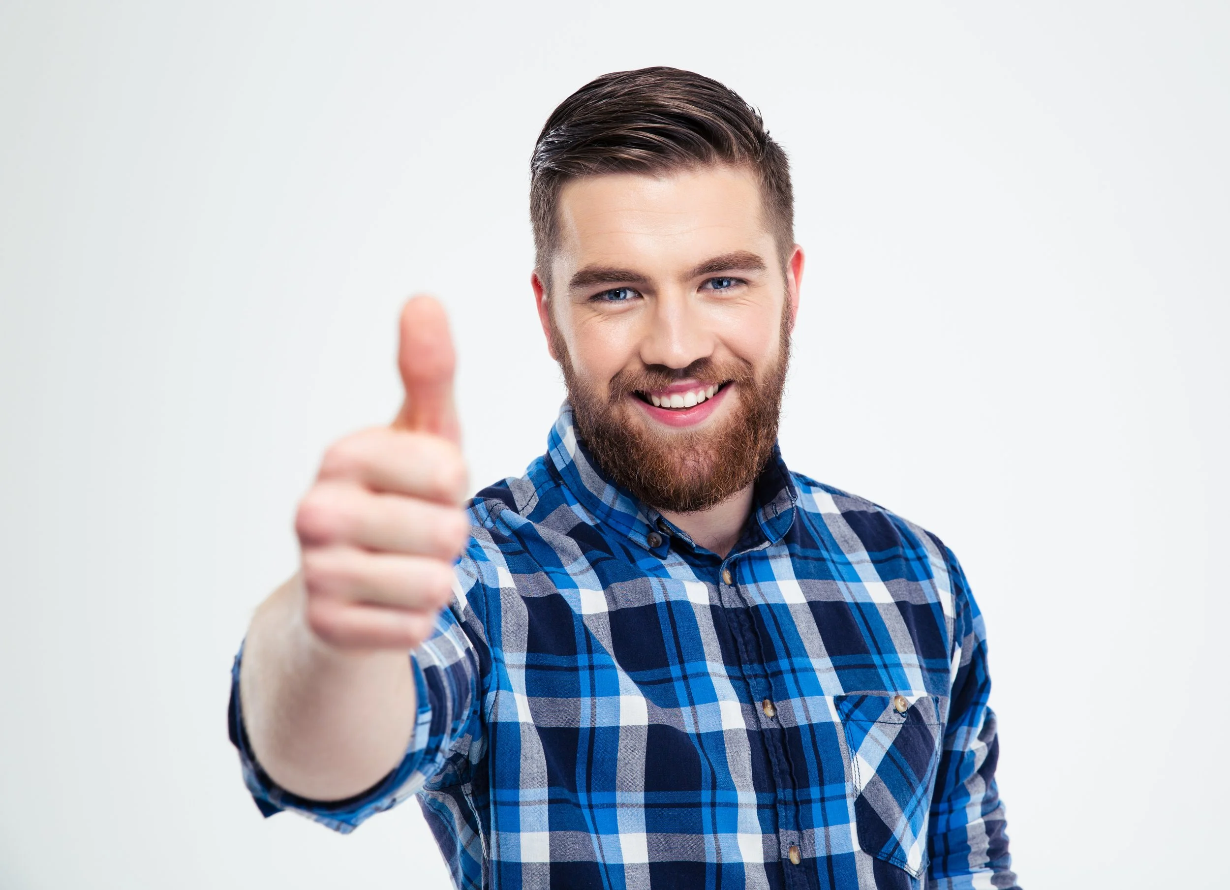 A smiling man with a beard and blue eyes giving a thumbs up, wearing a blue plaid shirt against a plain white background.