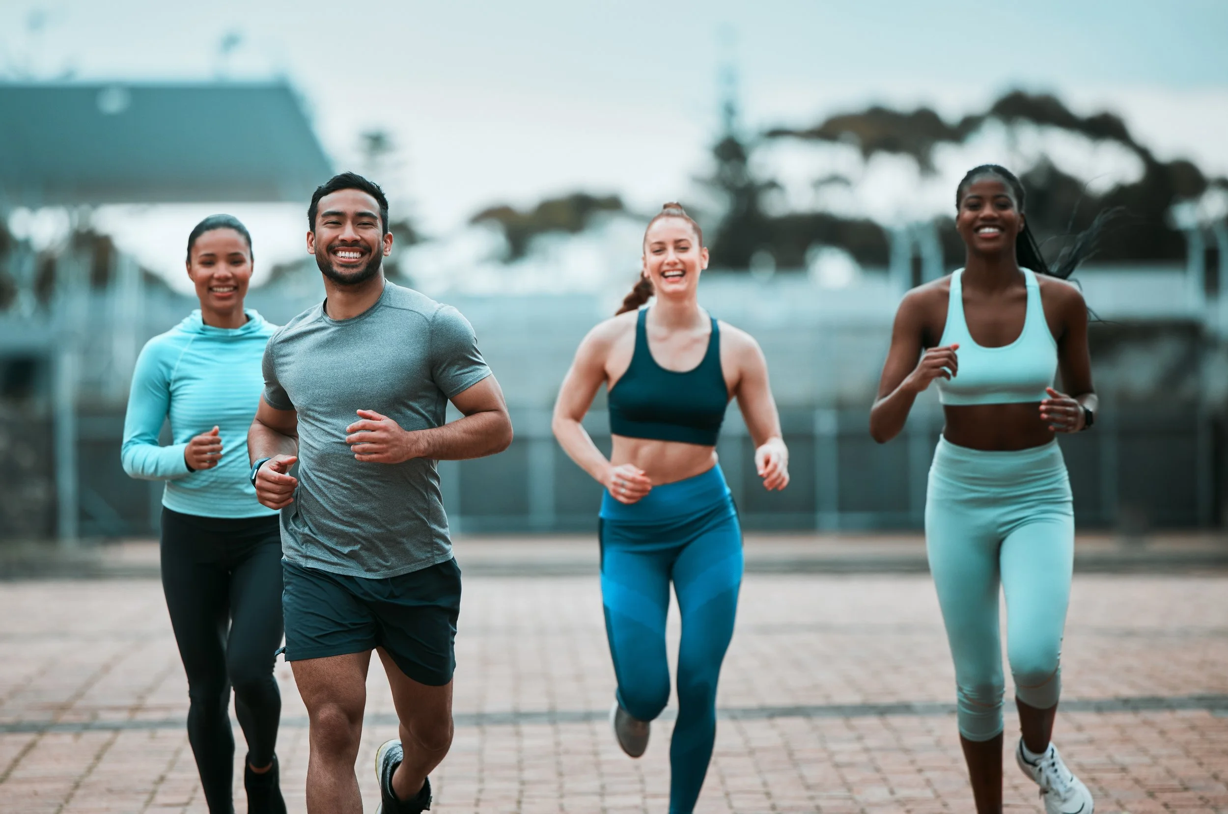 Four young adults running outdoors on a track, smiling and appearing energetic.